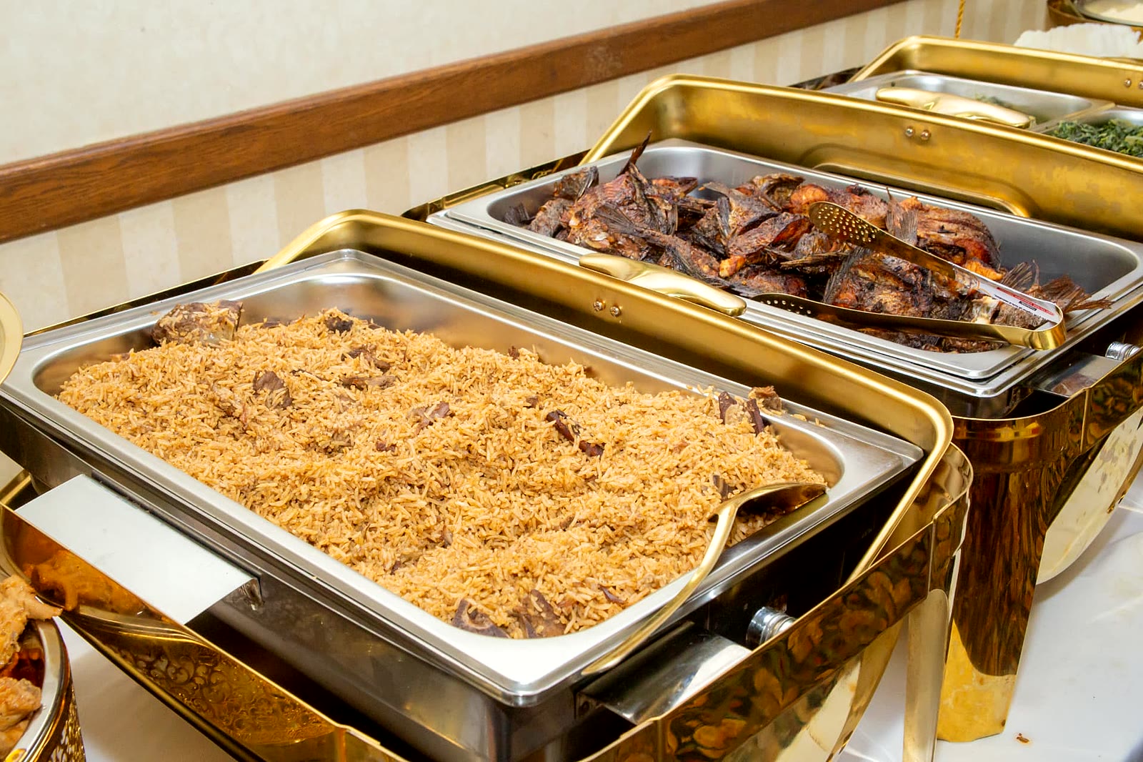 Trays of spiced pilau rice and deep-fried whole fish on a catering buffet in Toronto