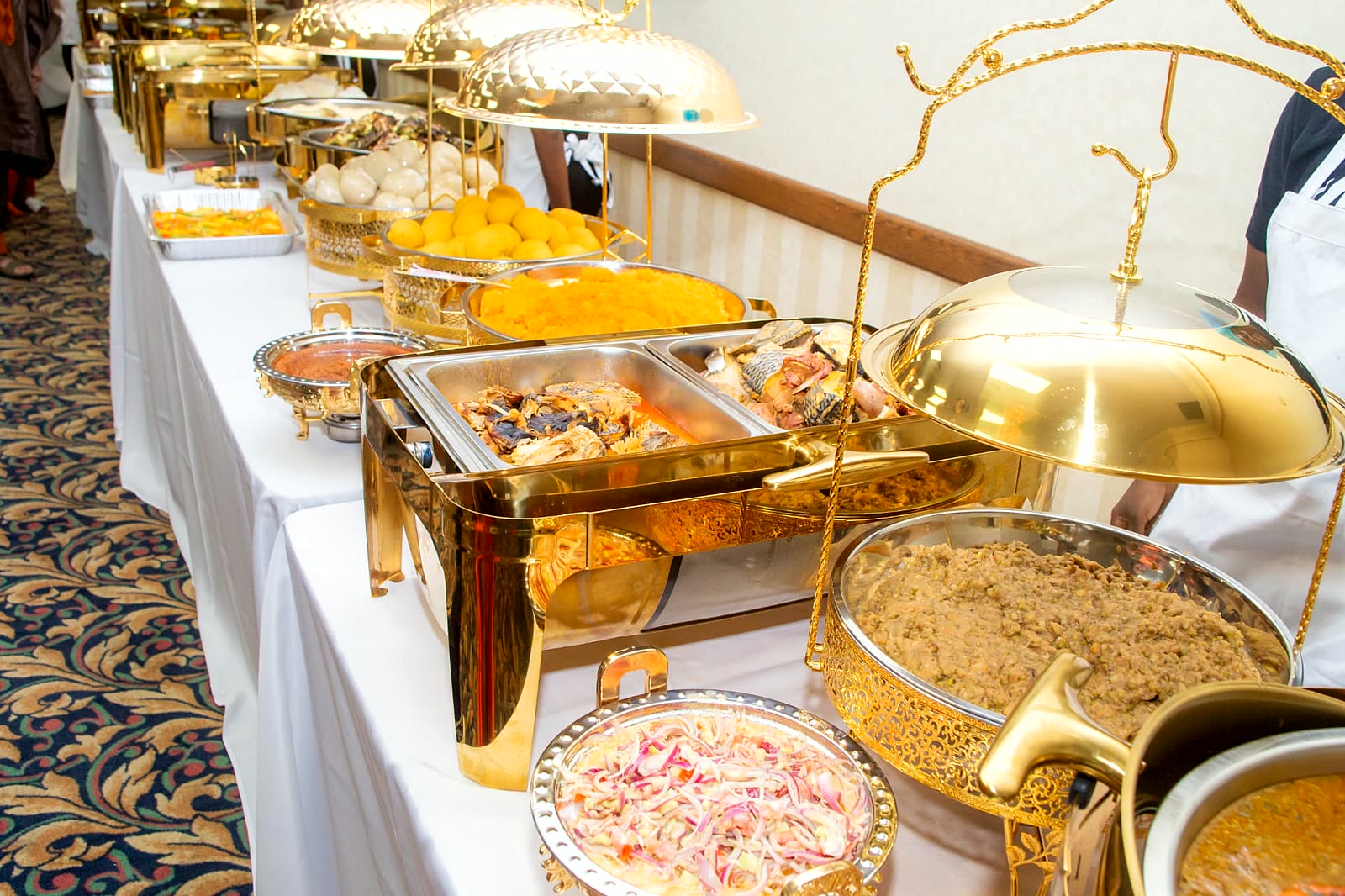 Extended buffet spread of fish, stews, salads and sides in gold chafing dishes at a Toronto celebration